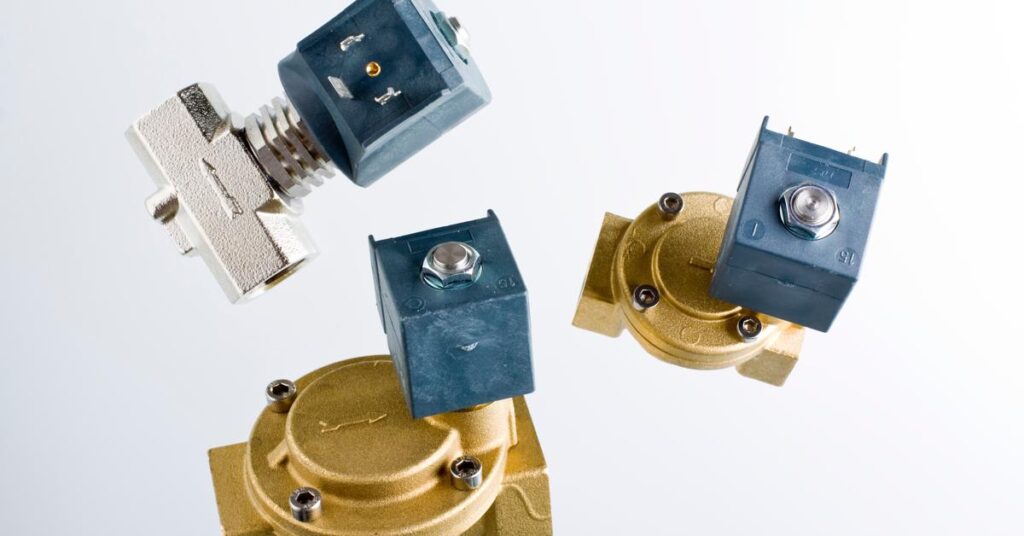 Three solenoid valves in front of a white background. Two valves are black and gold, and one valve is black and silver.