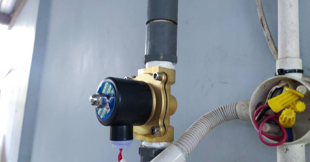  A solenoid valve attached to a water pressure pipe line. The pipes are gray and white, with red wires.