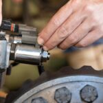 A close-up of a person handling different parts of a solenoid valve. A wheel is near the solenoid valve.