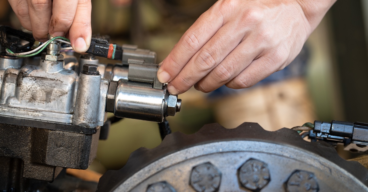 A close-up of a person handling different parts of a solenoid valve. A wheel is near the solenoid valve.
