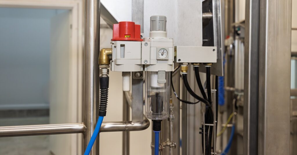 A pneumatic air filter system with tubes and a pressure gauge attaches to a metal structure inside an industrial facility.