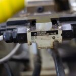 A solenoid-controlled valve with black connectors mounted to machinery and surrounded by cables and a large yellow hose.