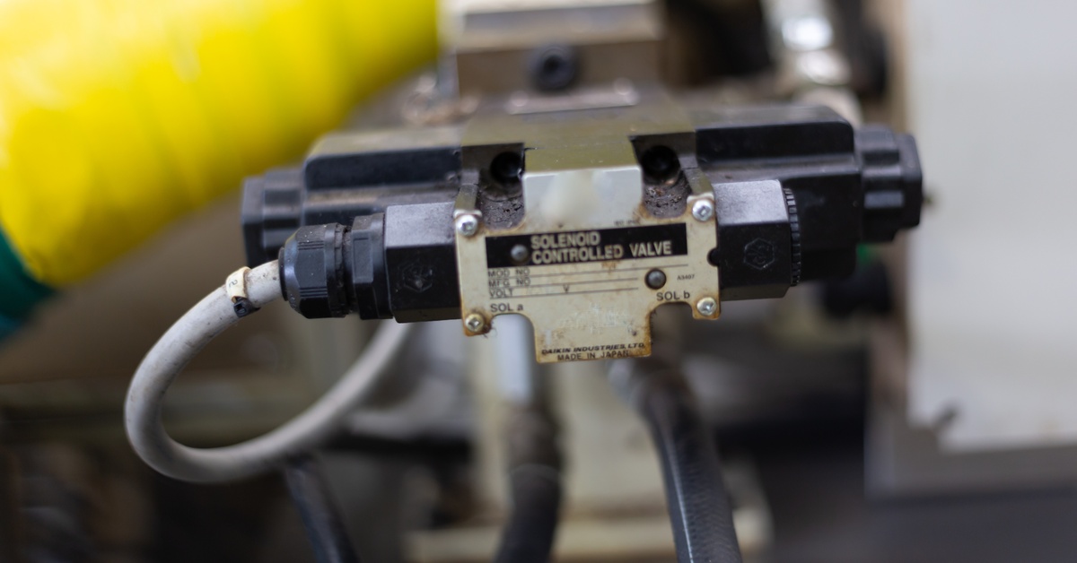 A solenoid-controlled valve with black connectors mounted to machinery and surrounded by cables and a large yellow hose.