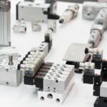 A display of components including solenoid valves, actuators, and connectors arranged on a white table.