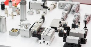 A display of components including solenoid valves, actuators, and connectors arranged on a white table.