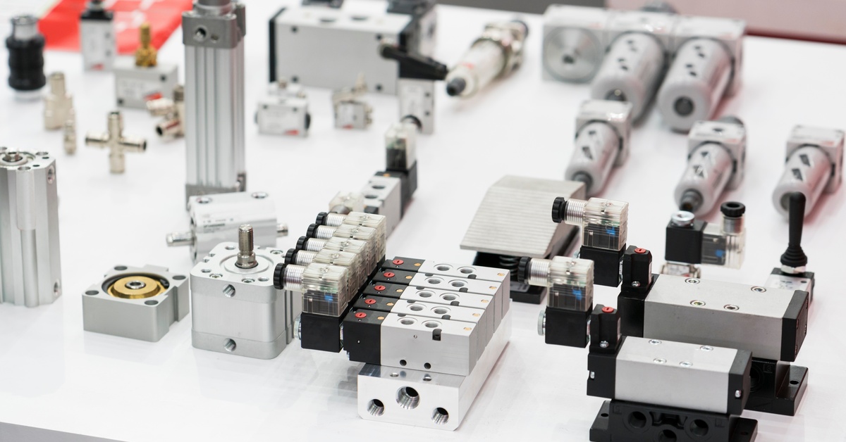 A display of components including solenoid valves, actuators, and connectors arranged on a white table.