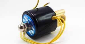 An industrial solenoid valve with yellow wires and a black cylindrical housing positioned against a plain white background.