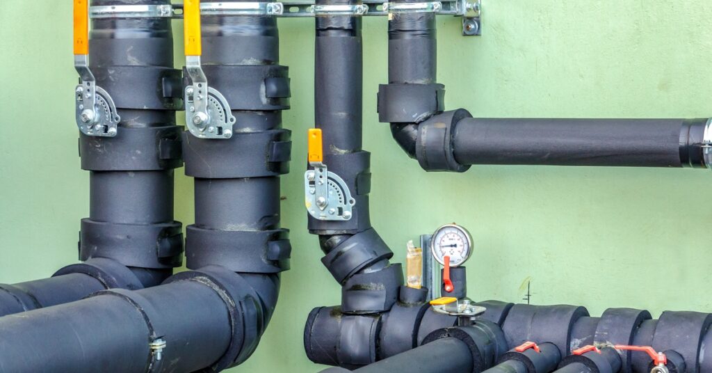 A wall-mounted network of black insulated plumbing pipes with visible gauges, valves, and metal brackets.