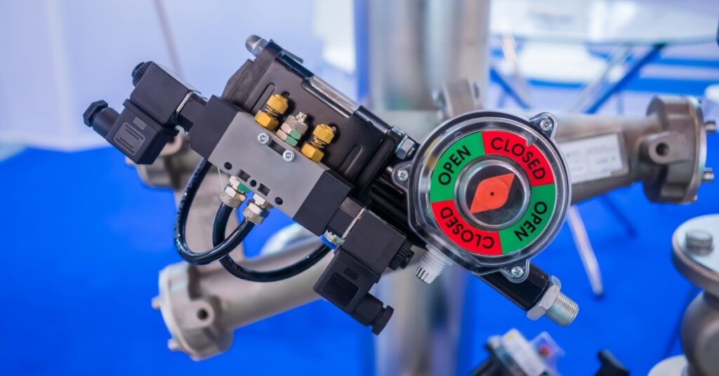 A blue industrial valve standing at the center of a large stainless steel piping system with control wiring.