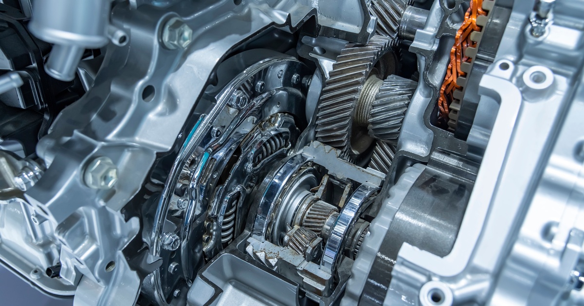 Metal gears are rotating inside an exposed automotive transmission system, with the teeth and housing structure visible.