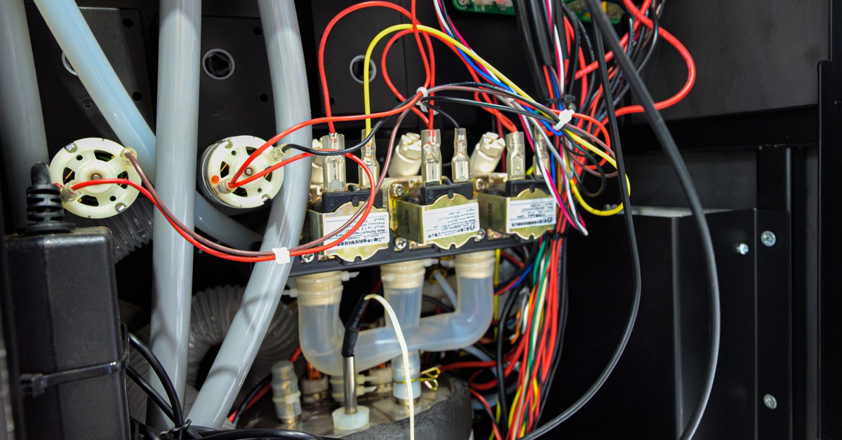A complex wiring harness connecting valves, tubes, and circuit boards inside an open black industrial equipment enclosure.