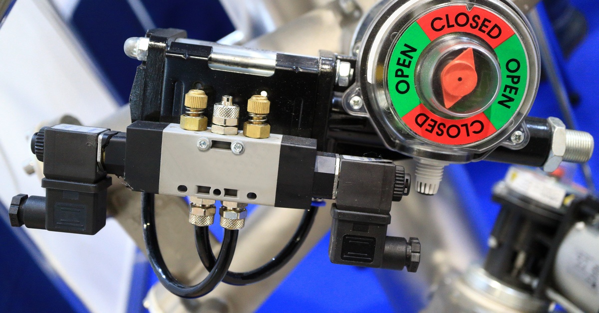 A mechanical valve actuator displaying directional labels while connecting tubing and electrical solenoid parts along the side.