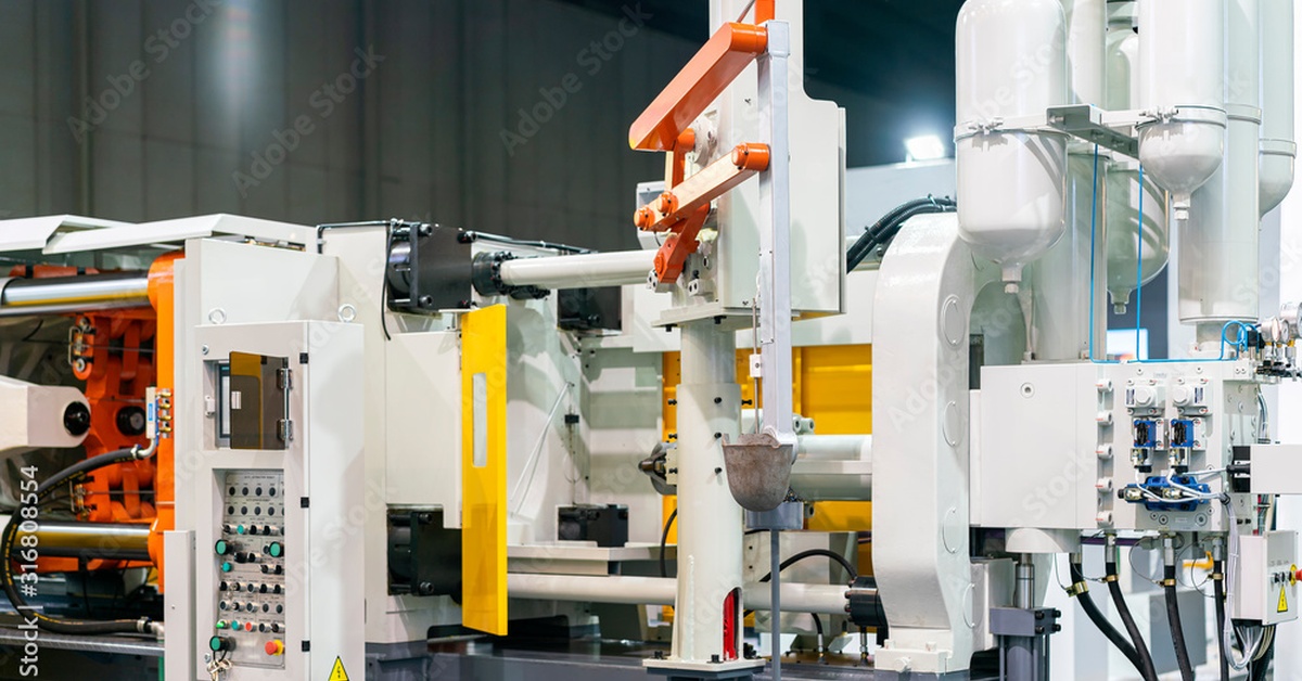 An automated die-casting machine with white tanks, control panels, and visible tubing throughout the system.