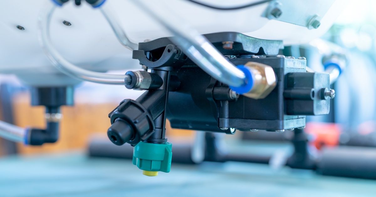 A black plastic nozzle connecting tubing beneath a mounted tank on a machine platform with a teal base.