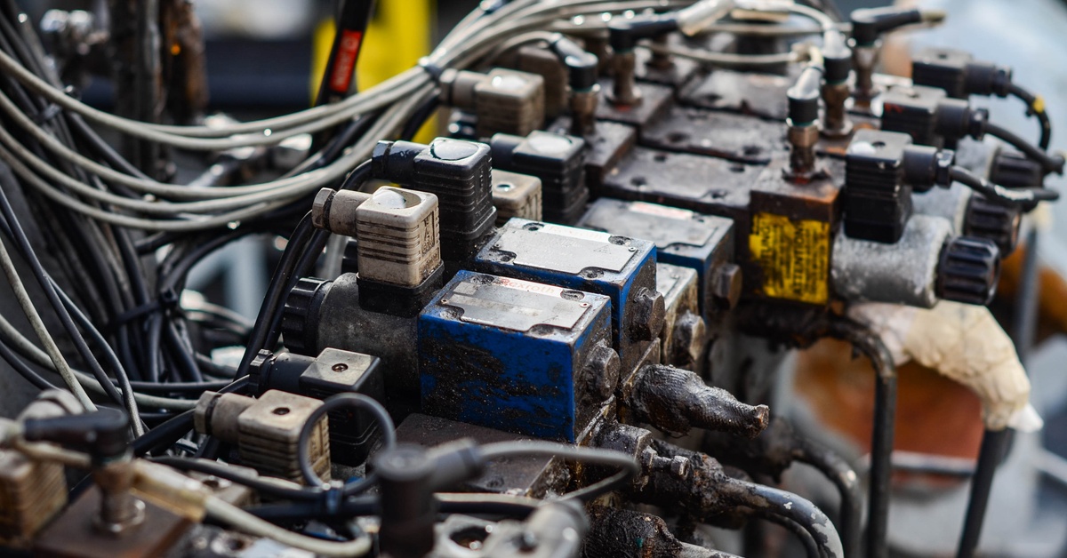 A row of solenoid valves mounted on a hydraulic machine panel with exposed wires and dark oil residue.