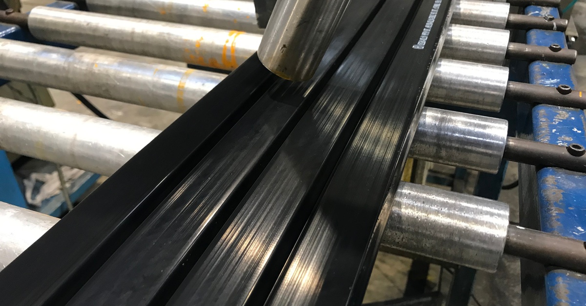 A heated nozzle heating up black plastic strips moving across metal rollers in an industrial production setting.