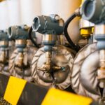 A row of industrial pressure transmitters with solenoids inside a brightly lit facility with yellow safety railings.