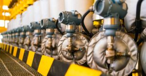 A row of industrial pressure transmitters with solenoids inside a brightly lit facility with yellow safety railings.