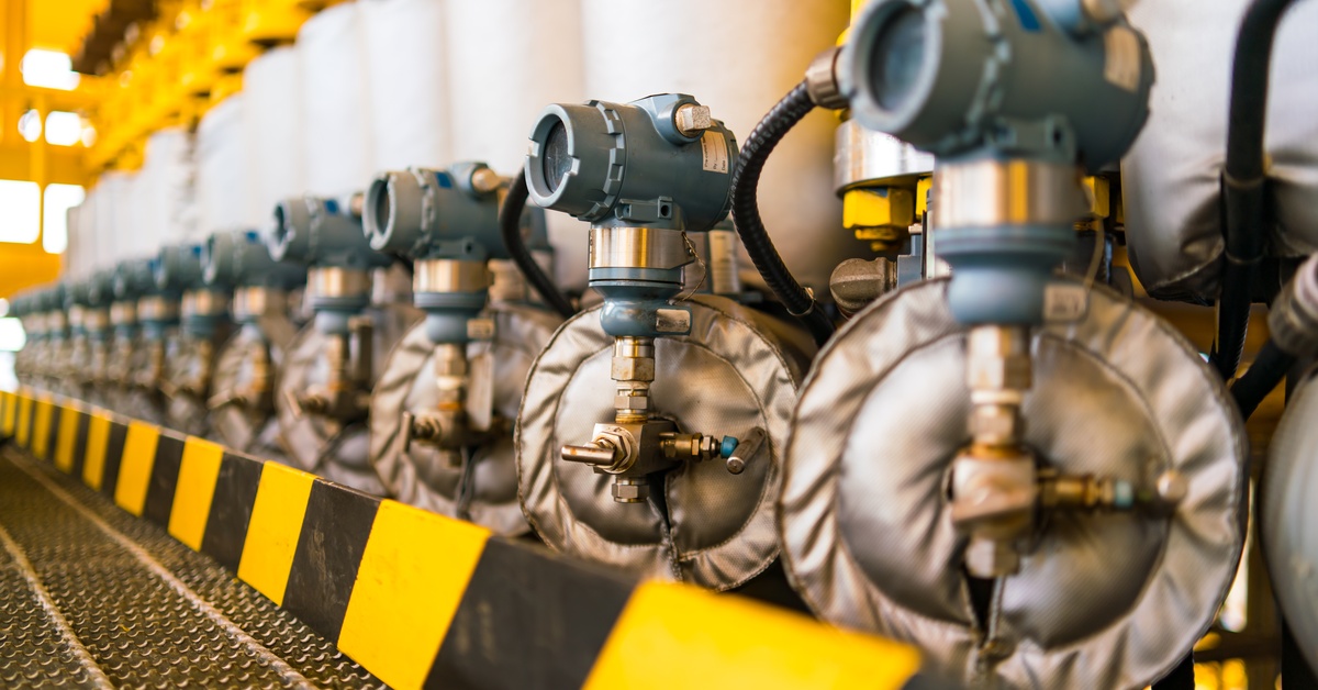 A row of industrial pressure transmitters with solenoids inside a brightly lit facility with yellow safety railings.