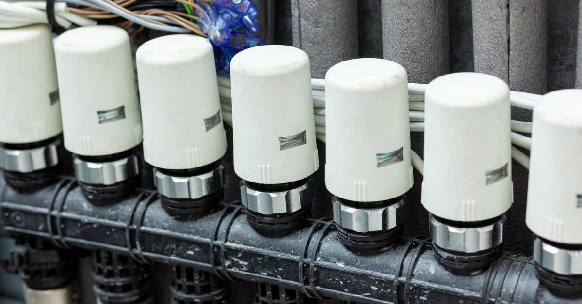 A row of white valve actuators mounted on a black manifold with insulated pipes and connected electrical wiring above.