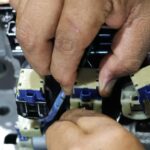 A close-up view shows a technician's hands touching a blue and white solenoid on a control valve.