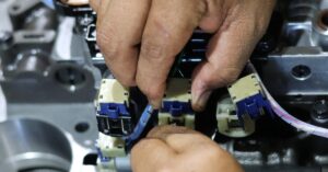 A close-up view shows a technician's hands touching a blue and white solenoid on a control valve.