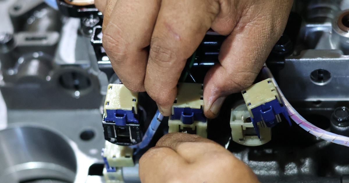 A close-up view shows a technician's hands touching a blue and white solenoid on a control valve.