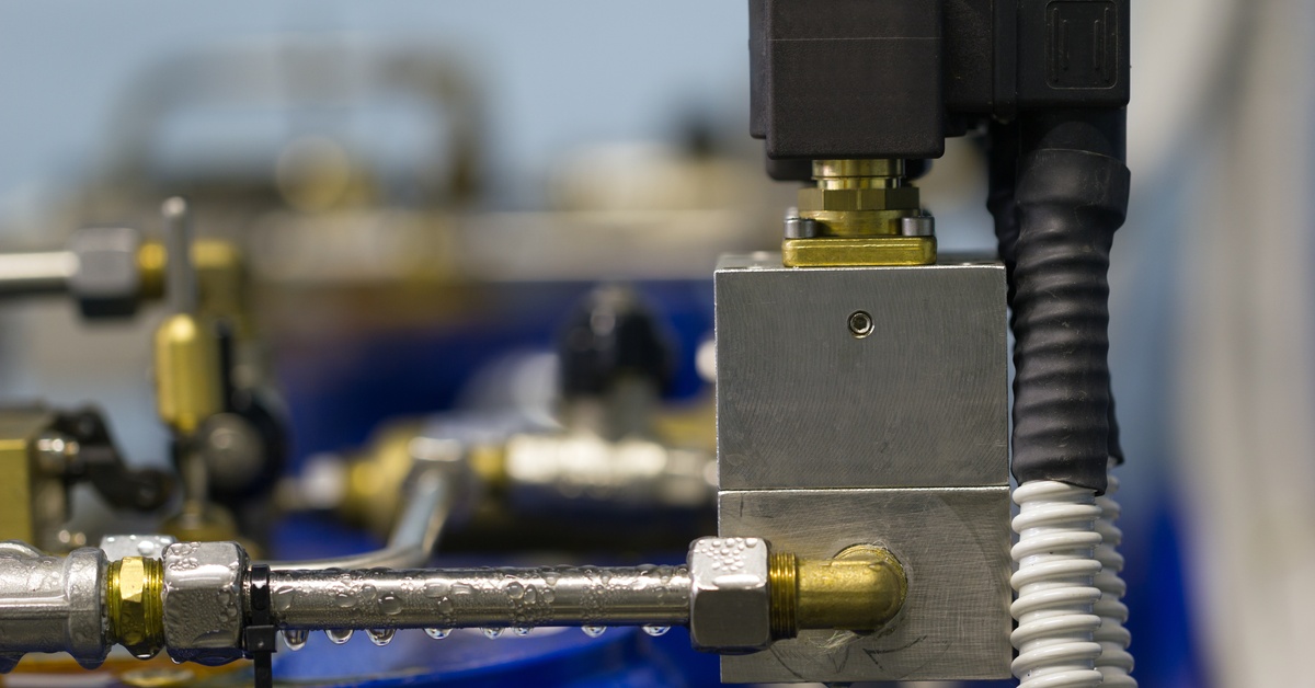 A close-up view shows a blue, black, and gold electrical solenoid valve. Condensation drips off the part.