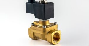 A single solenoid valve sits on a white background. The valve has a brass bottom with a black top.