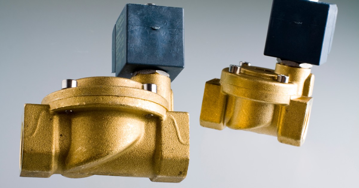 Two brass and black solenoid valves sit against a gradient gray background. One valve is closer than the other.