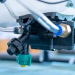 A close-up view shows a black solenoid valve with three clear, plastic hoses attached to it with brass couplings.