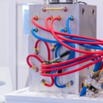 A metal molding machine sits in an industrial setting with several blue and red tubes coming out of the sides.