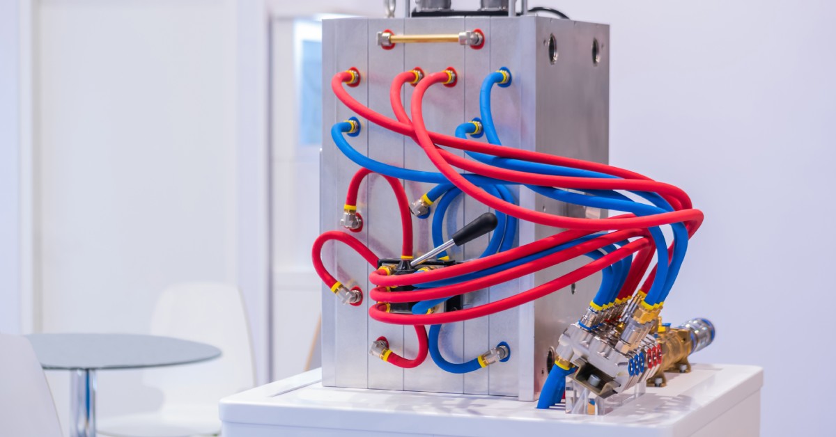 A metal molding machine sits in an industrial setting with several blue and red tubes coming out of the sides.