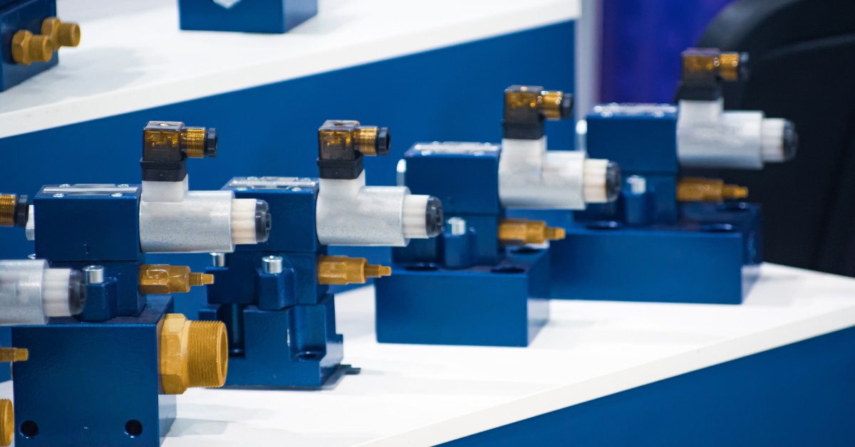 A row of blue industrial solenoid valves with brass and steel fittings displayed on a white surface at an equipment showcase.