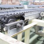 A large industrial conveyor belt sits in an industrial warehouse. Cardboard boxes are in the background.
