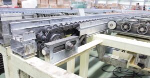 A large industrial conveyor belt sits in an industrial warehouse. Cardboard boxes are in the background.
