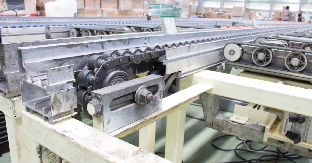 A large industrial conveyor belt sits in an industrial warehouse. Cardboard boxes are in the background.