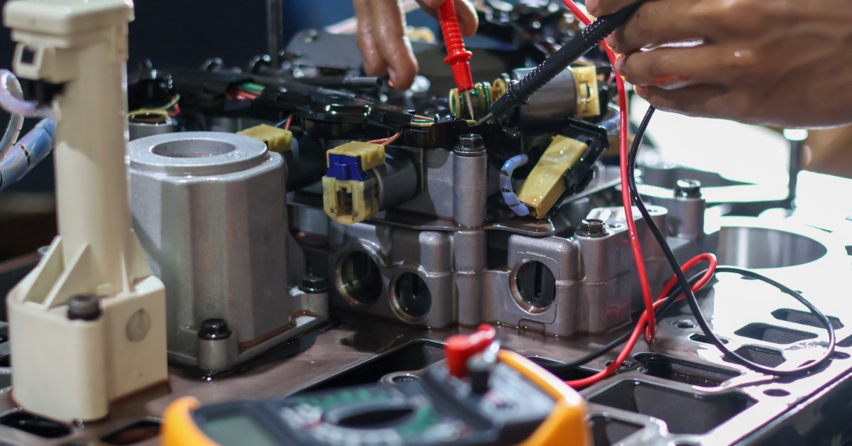 A close-up view shows a person holding a red and a black electrical tool working on a solenoid valve.