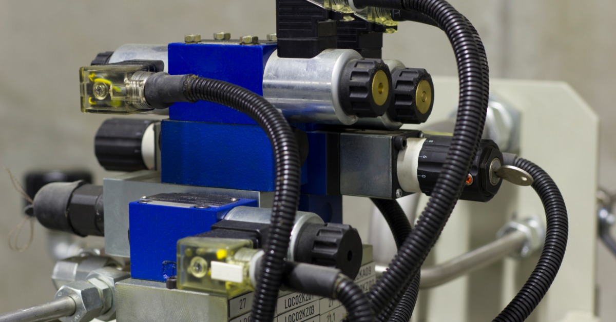 Several black tubes are coming out of various locations of a blue and gray hydraulic solenoid valve system.