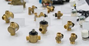 A white table features various bronze solenoid valves and pipes for industrial parts. The valves have black tops.