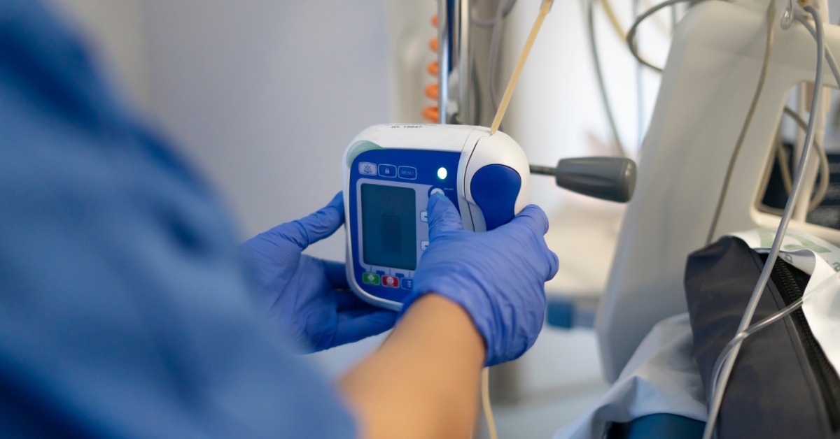 A close-up view shows a medical professional wearing blue scrubs and blue latex gloves pressing buttons on a pump machine.