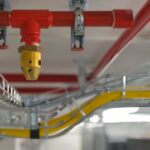 A skinny, red pipe is attached to the ceiling with metal brackets. A brass sprinkler comes out of the red pipe.