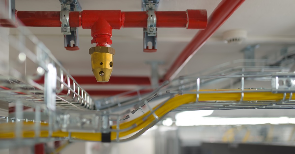 A skinny, red pipe is attached to the ceiling with metal brackets. A brass sprinkler comes out of the red pipe.