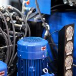 A hydraulic system features blue metal, gray tubes, and several pressure gauges. A zip tie keeps the tubes organized.