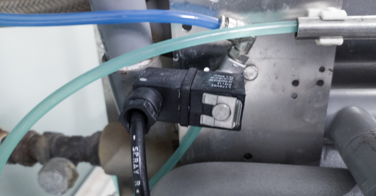A close-up view shows two clear, plastic tubes next to a metal machine. One tube has a blue liquid, and one has a teal liquid.