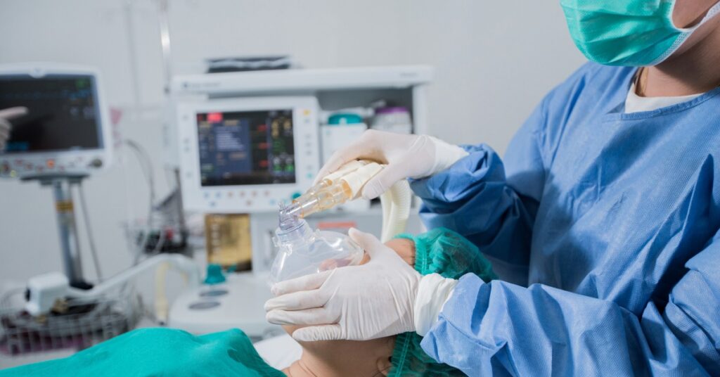 A medical professional is placing an anesthesia gas mask on a patient who's lying on an operating table for surgery.